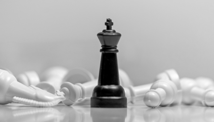 A black chess king standing among fallen white pieces